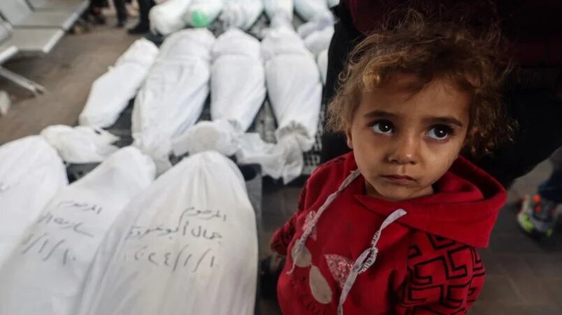 A Palestinian child stands near the bodies of family members killed during an Israeli bombardment in Rafah, Gaza, on 10 January 2024 (AFP)