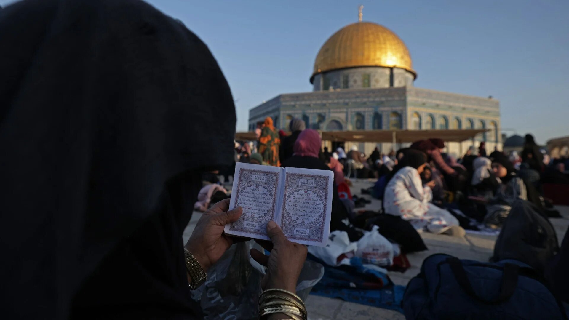 A Muslim woman reads from the Quran outside the Dome of the Rock in Jerusalem's Al-Aqsa Mosque compound on 17 April 2023 (Hazem Bader/AFP)