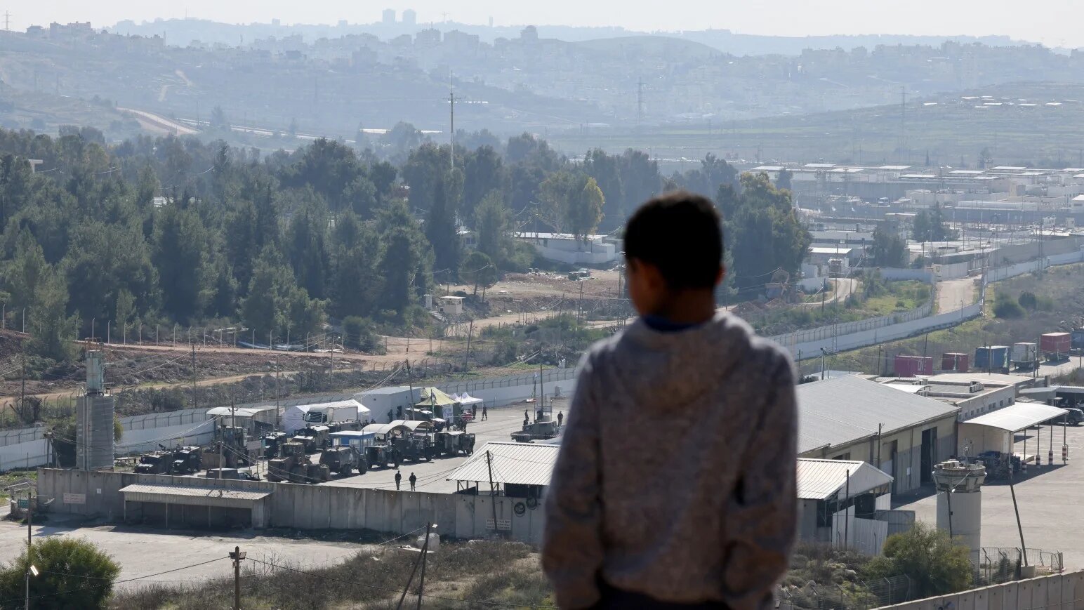 A Palestinian boy watches from a hilltop as Israeli troops gather with their vehicles inside the Ofer military prison complex, located between Ramallah and Beitunia in the occupied West Bank, before releasing Palestinian prisoners as part of a third hostage-prisoner exchange on 30 January 2025 (AFP)