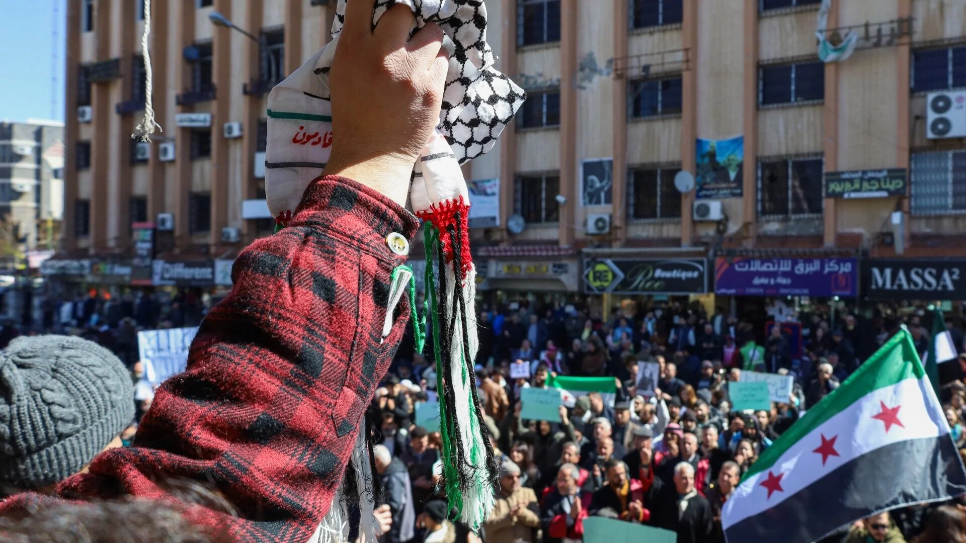 A protester lifts a Palestinian keffiyeh as Syrians demonstrate in the central Karama Square of the southern city of Sweida on 25 February 2025 (Shadi al-Dubaisi)