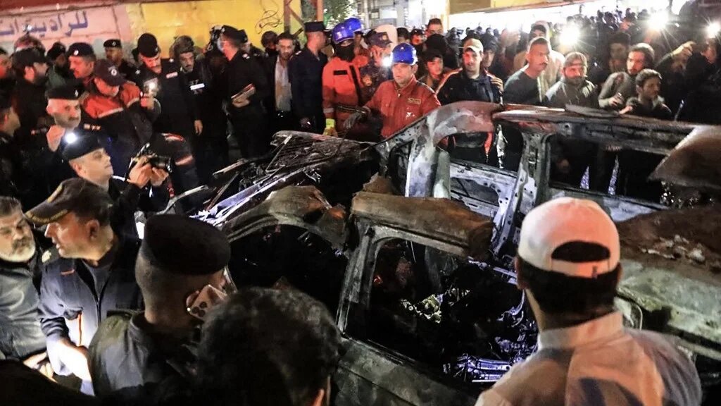 People gather around a vehicle hit by a drone strike, reportedly killing three people, including two leaders of a pro-Iran group, Baghdad, 7 February 2024 (Murtaja Lateef/AFP)