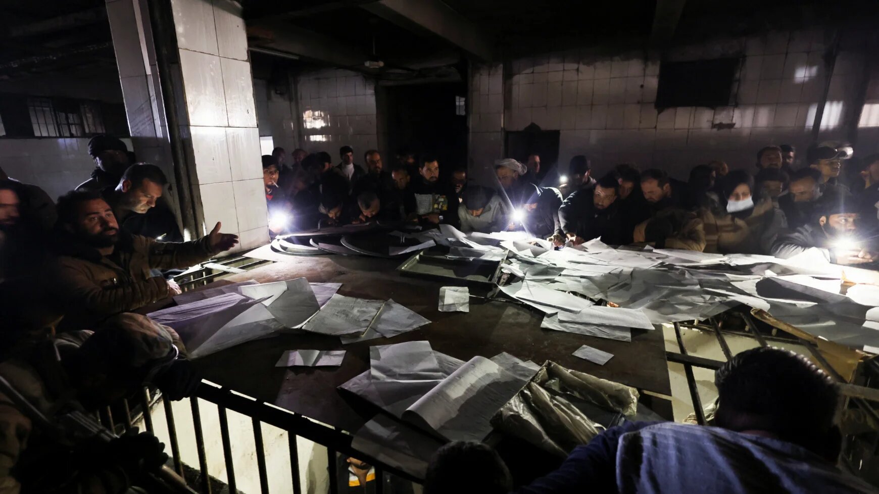 People search through papers as they join members of the Syrian civil defence group, known as the White Helmets, to search for prisoners underground at Sednaya prison on 9 December 2024 (Amr Abdallah Dalsh/Reuters)
