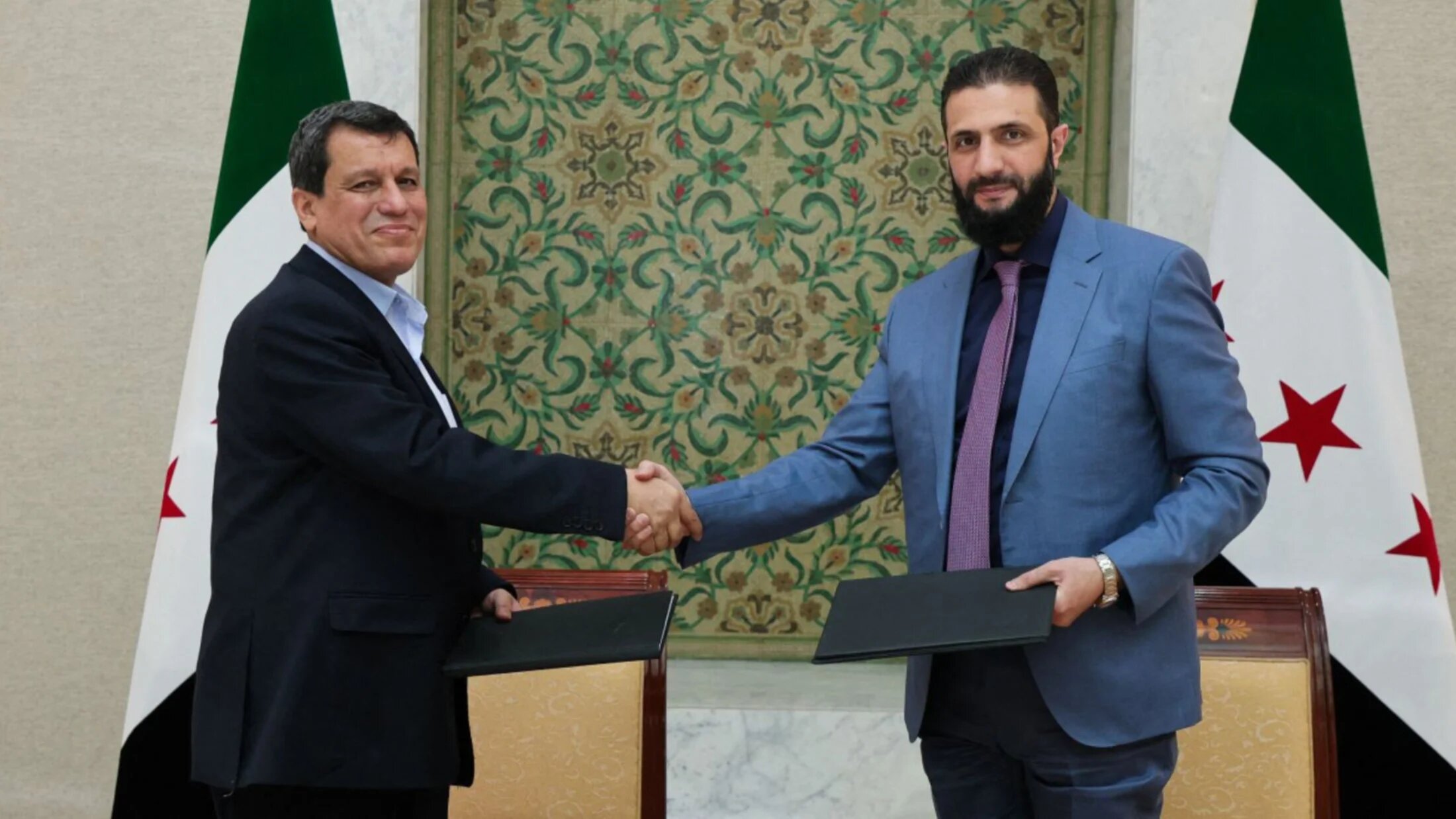 Syria's interim president Ahmed al-Sharaa (R) shakes the hand of Syrian Democratic Forces commander-in-chief Mazloum Abdi Shaheen after the signing of an agreement in Damascus on 10 March 2025 (SANA/AFP)