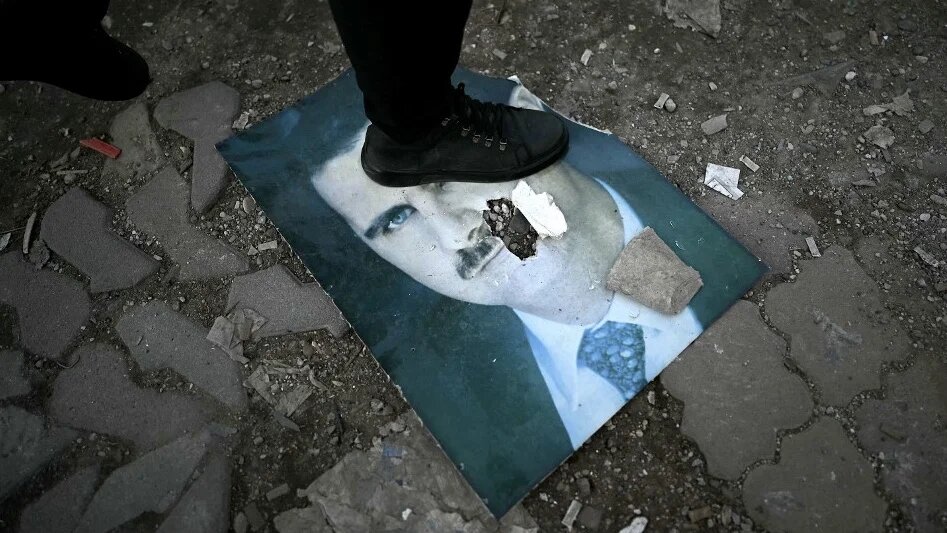 A man steps on a portrait of Syria's ousted President Bashar al-Assad in the Syrian port city of Latakia on 15 December 2024 (Ozan Kose/AFP)