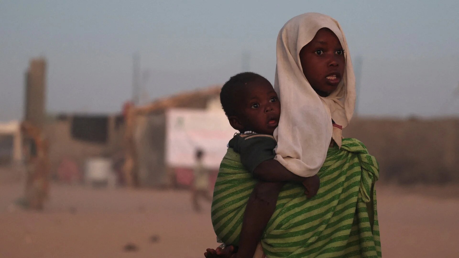A Sudanese refugee girl from el-Fasher carries her brother at the Tine transit refugee camp in eastern Chad, 21 November 2025 (Reuters/Amr Abdallah Dalsh)