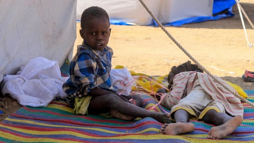 Children from el-Fasher rest outside their tent at a camp for displaced Sudanese people in the northern town of al-Dabba on 13 November 2025 (AFP)