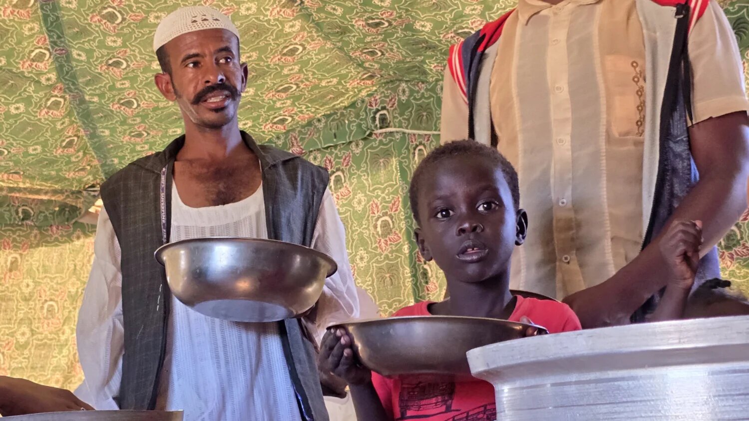 A child and a man wait to collect food at a location set up by a local humanitarian organisation to donate meals and medication to displaced people in Meroe, Sudan on 9 January 2025 (AFP)