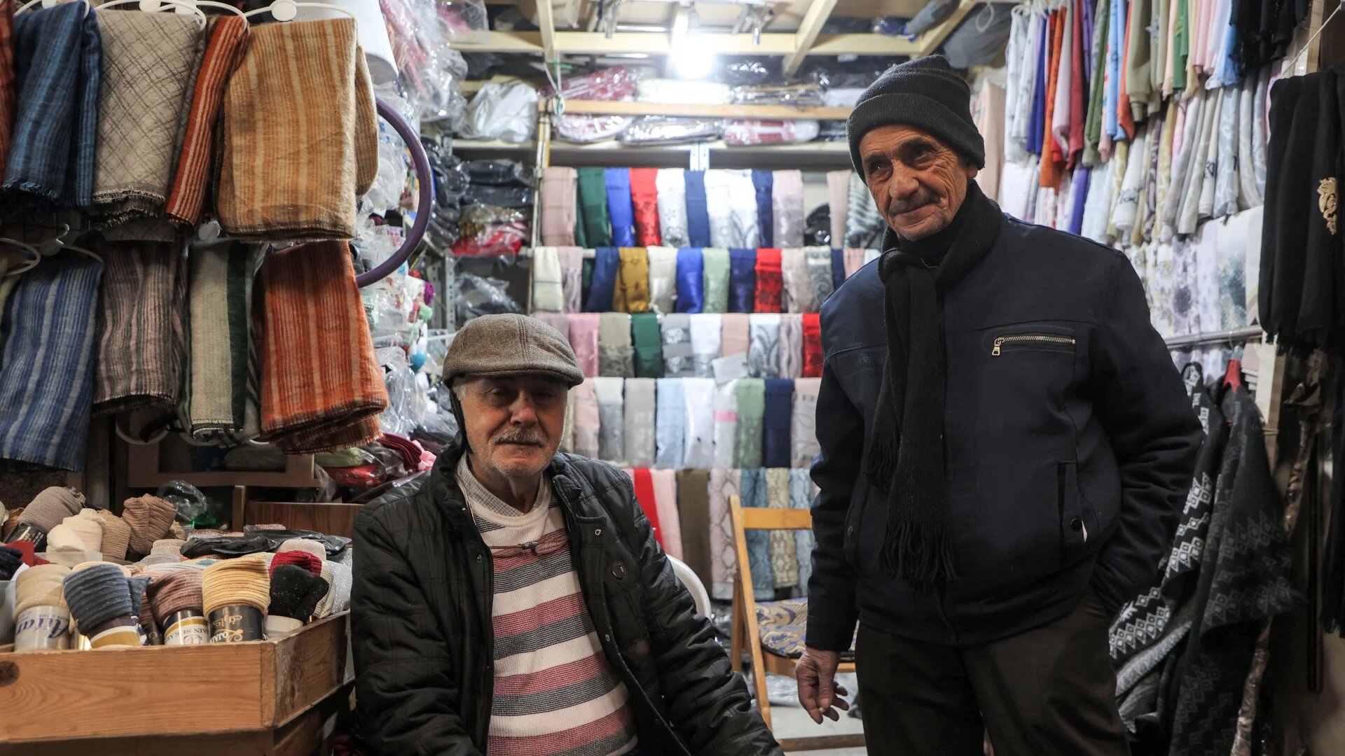 Vendors sit outside a clothing shop along an alley of the covered market in the old city of Homs on 16 December 2024 (Aaref Watad/AFP)