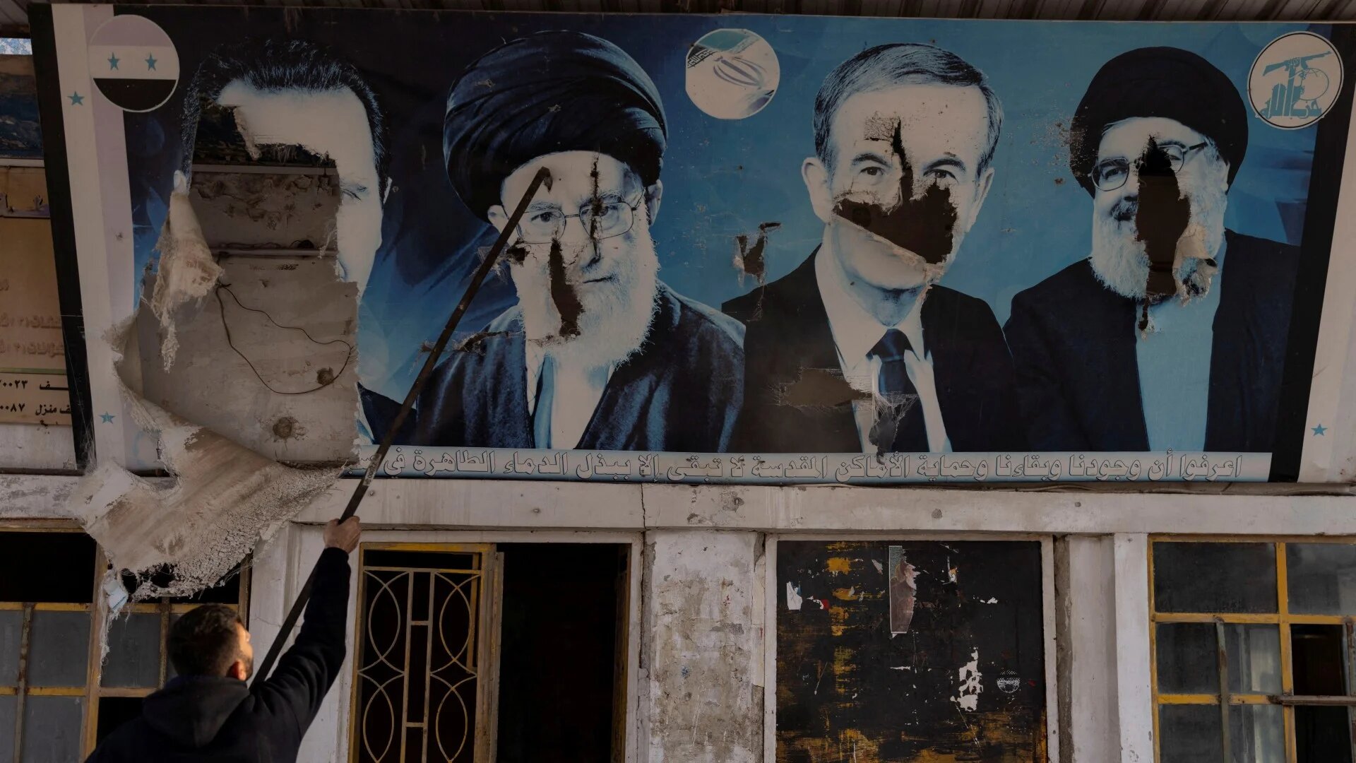 A worker tears down portraits of Bashar al-Assad, Hafez al-Assad, former Hezbollah leader                                                                                                                                                                                          Hassan Nasrallah and Iranian Supreme Leader Ali Khamenei at a gas station in Nubl on 11 December 2024 (Reuters/Umit Bektas)