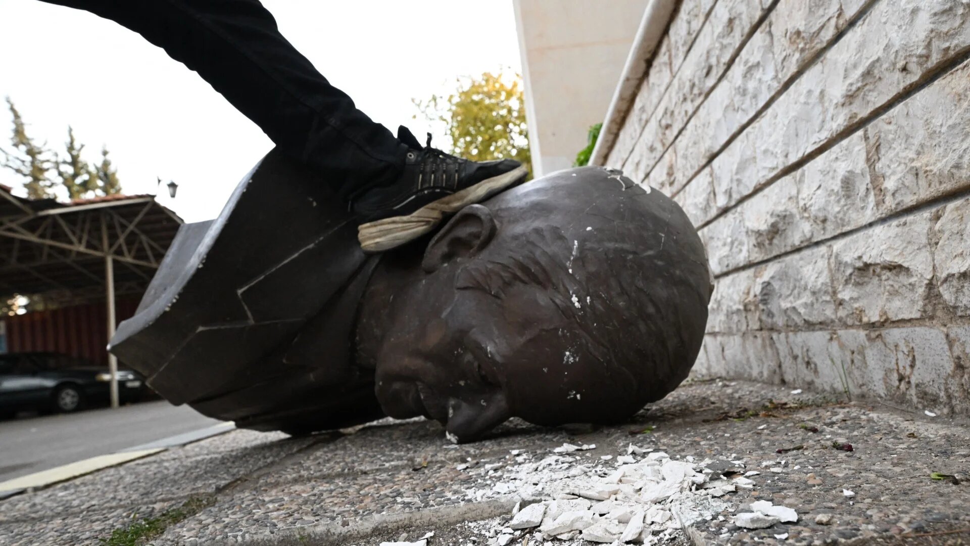 An anti-government fighter treads on a statue of late Syrian president Hafez al-Assad that was felled outside the defence ministry's military security headquarters in the Damascus district of Kafr Sousa on 9 December 2024 (AFP)