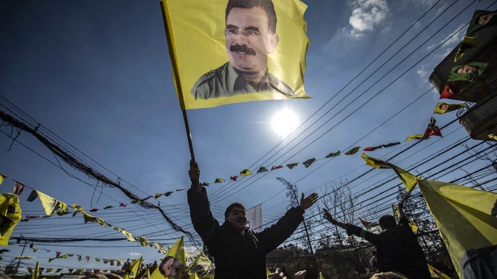 A protester waves a flag bearing a portrait of Abdullah Ocalan, the jailed PKK leader, during a demonstration in northeastern Syria on 15 February 2025 (Delil Souleiman/AFP)