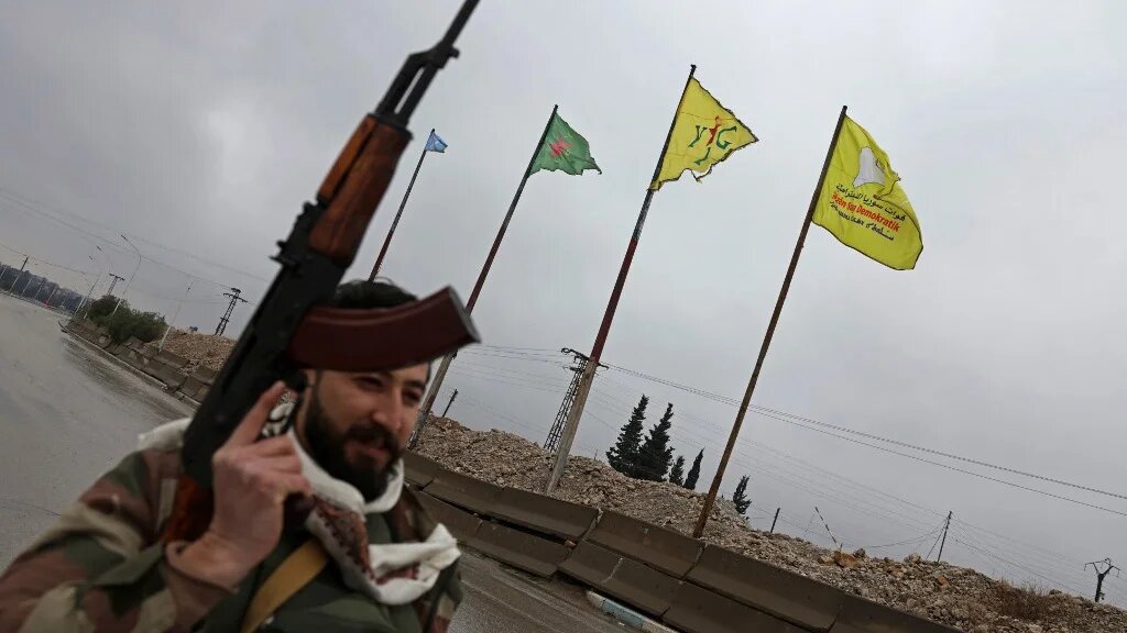 A member of the Syrian army walks past YPG flags in Tabqa on 18 January 2026 (Bakr Alkasem/AFP)