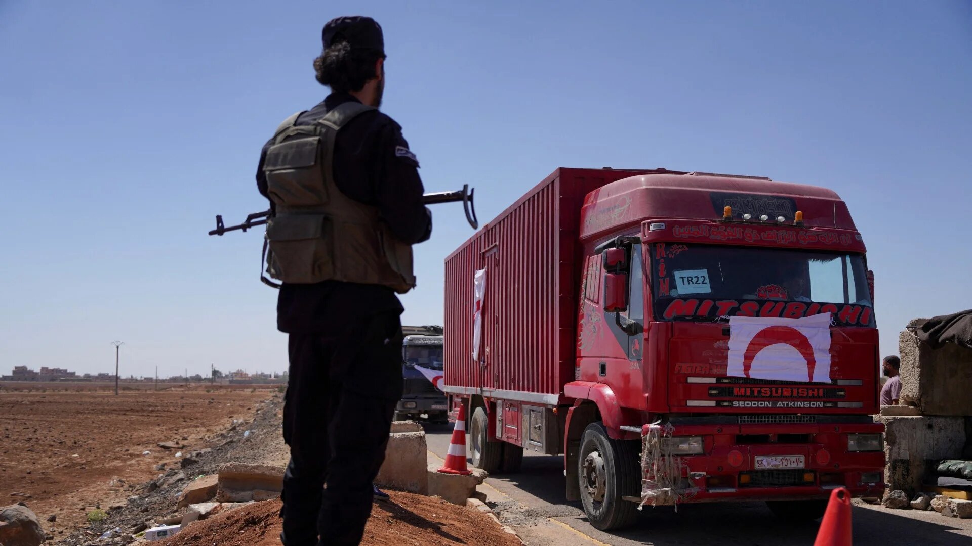 A member of Syrian security forces stands near a vehicle carrying aid as they make their way to Sweida, at Bosra al-Sham, Syria 23 July 2025 (Reuters/Karam al-Masri)