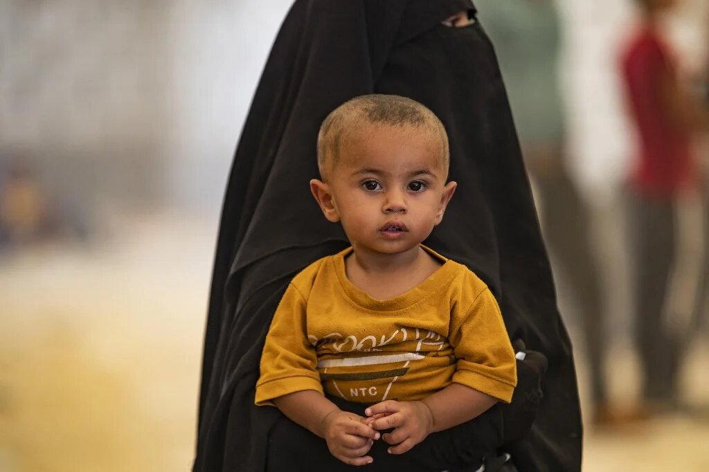 Une femme porte son enfant alors que les Syriens attendent d’être libérés du camp kurde d’al-Hol, dans le Nord-Est du gouvernorat d’Hassaké, le 14 août 2022 (AFP/Delil Souleiman)