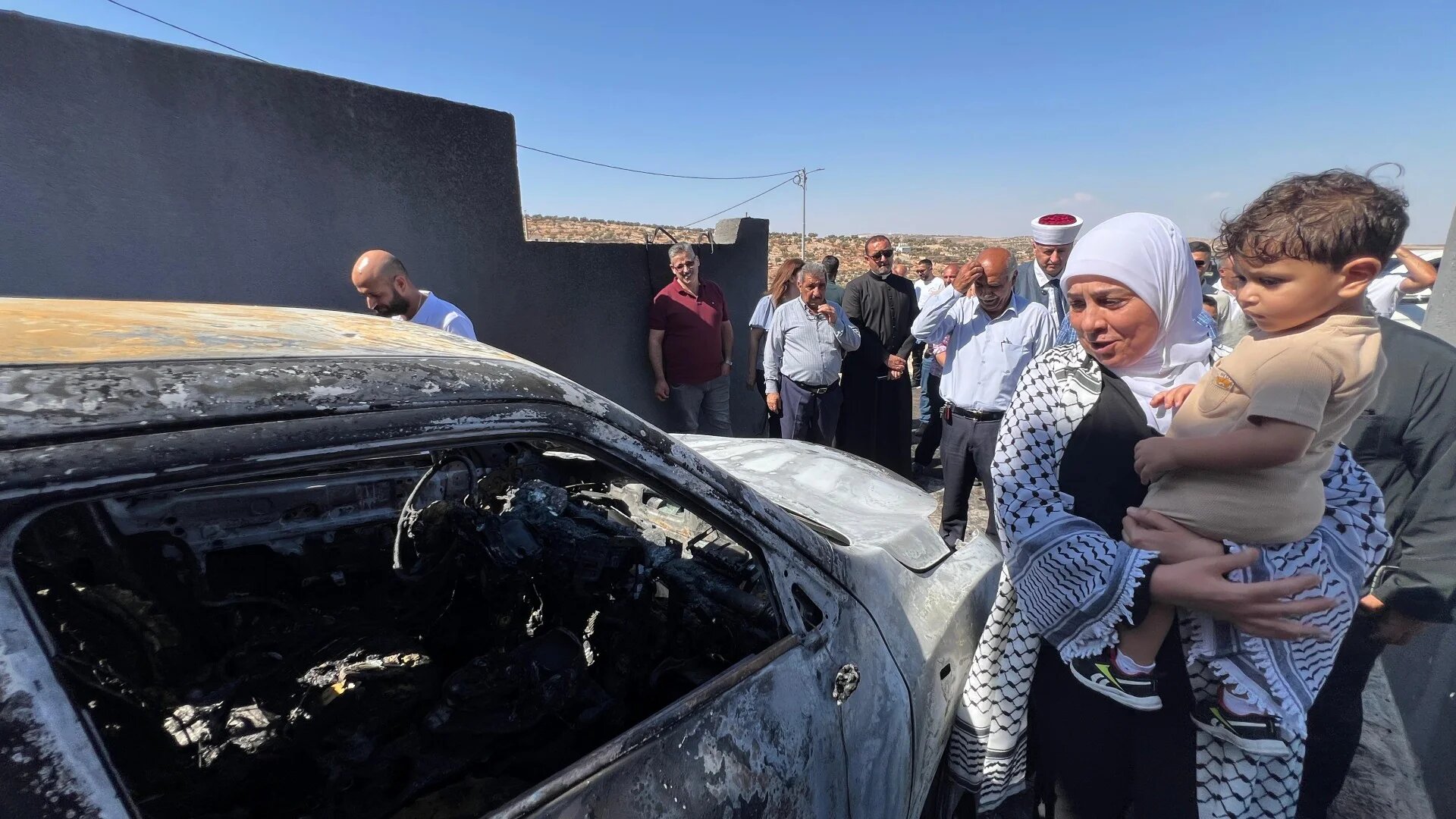 A woman and child look at remains of a car set alight by Israeli settlers in Taybeh on 28 July (Mohammed Turkman/MEE)