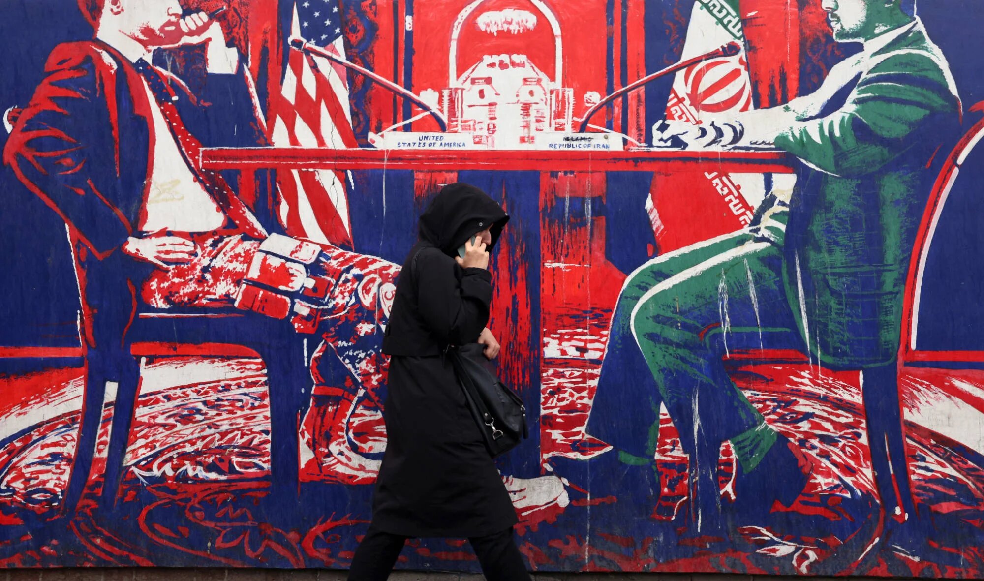 A woman walks past a mural painted on the outer wall of the former US Embassy in Tehran, dubbed the 'Den of Espionage', on 8 March 2025 (AFP)