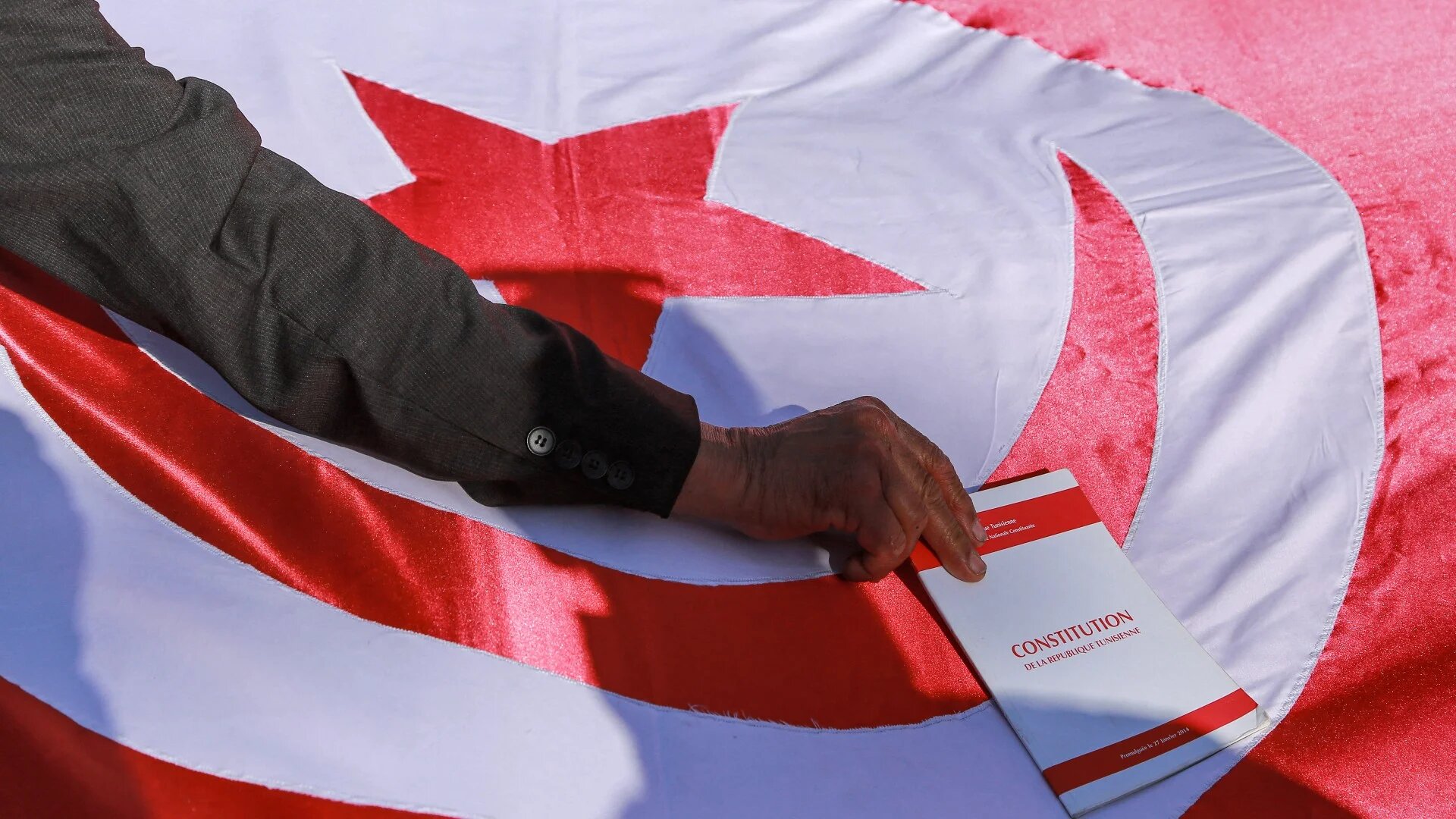 A man places a copy of the Tunisian constitution atop a Tunisian national flag during a demonstration called against President Kais Saied on 13 February 2022 (AFP)
