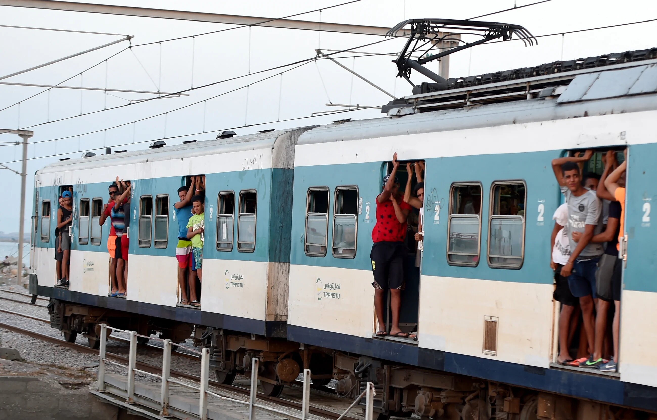 Tunisian youths look out of the doors of a train linking the port city of La Goulette with Tunis on the outskirts of the Tunisian capital on 12 July 2016.
