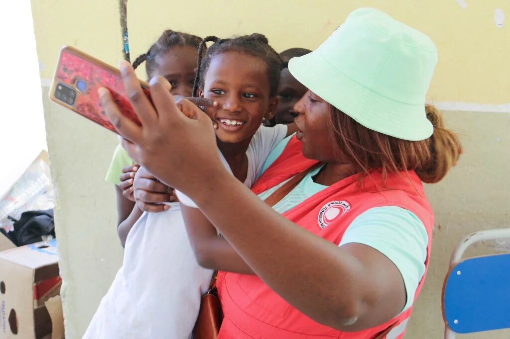 Une membre du Croissant-Rouge tunisien prend un selfie avec de jeunes migrants qui ont fui les violences à Sfax (est) vers la zone tampon militarisée entre la Tunisie et la Libye, et ont été accueillis dans un internat de Ben Guerdane, le 12 juillet 2023 (AFP/Fathi Nasri)
