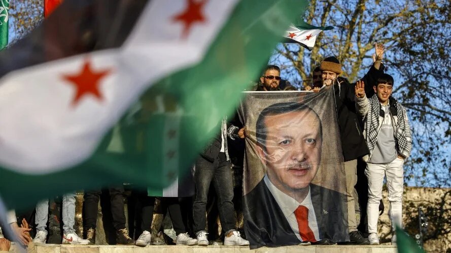 People hold a banner of Turkish President Recep Tayyip Erdogan as members of the Syrian community mark the fall of the Assad regime, in Istanbul on 8 December 2024 (Kemal Aslan/AFP)