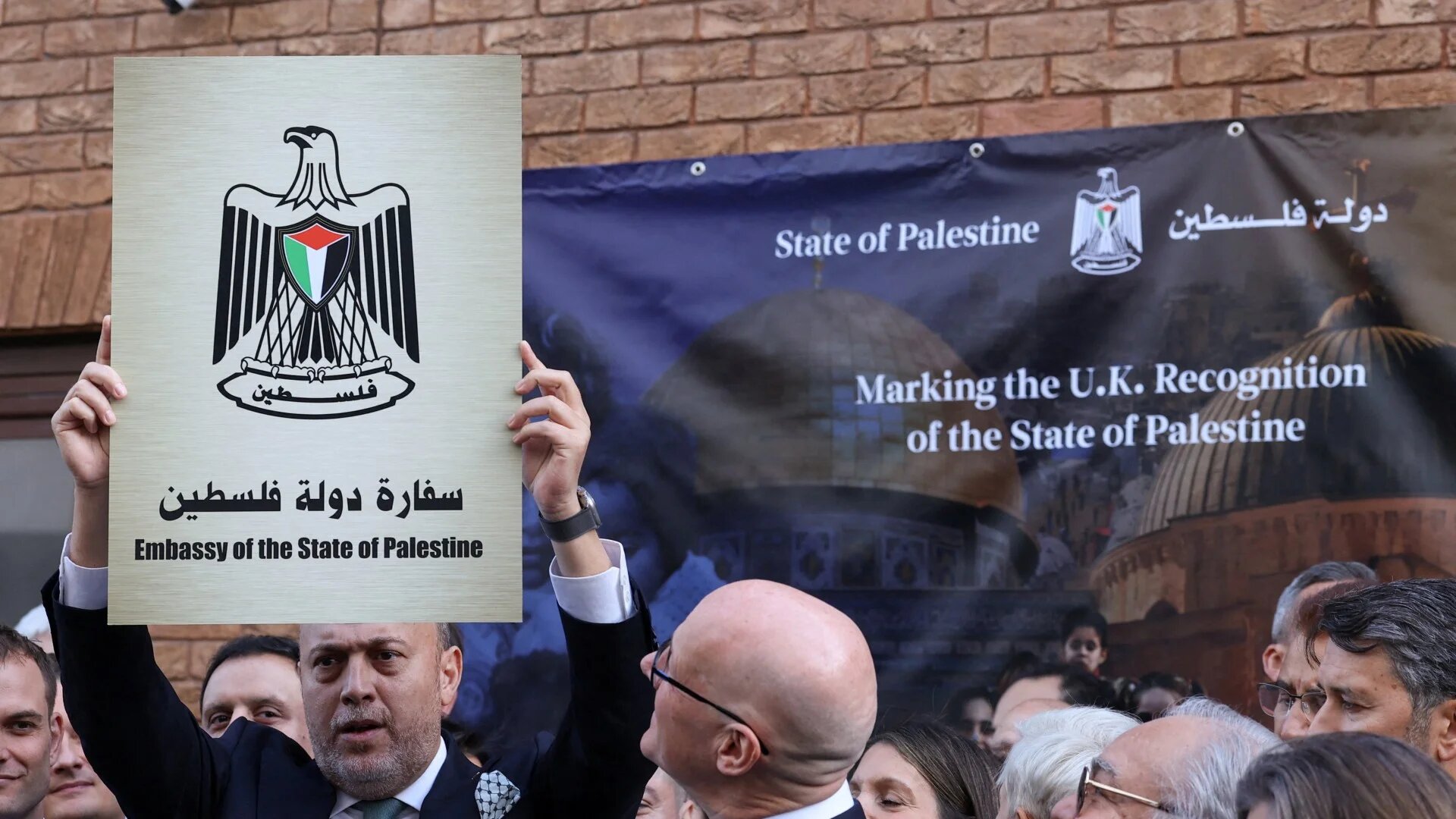 Husam Zomlot, the presumptive Palestinian Ambassador to the UK, holds up a plaque which reads "Embassy of the State of Palestine" during a flag raising ceremony in London on 22 September 2025 (Toby Melville/Reuters)