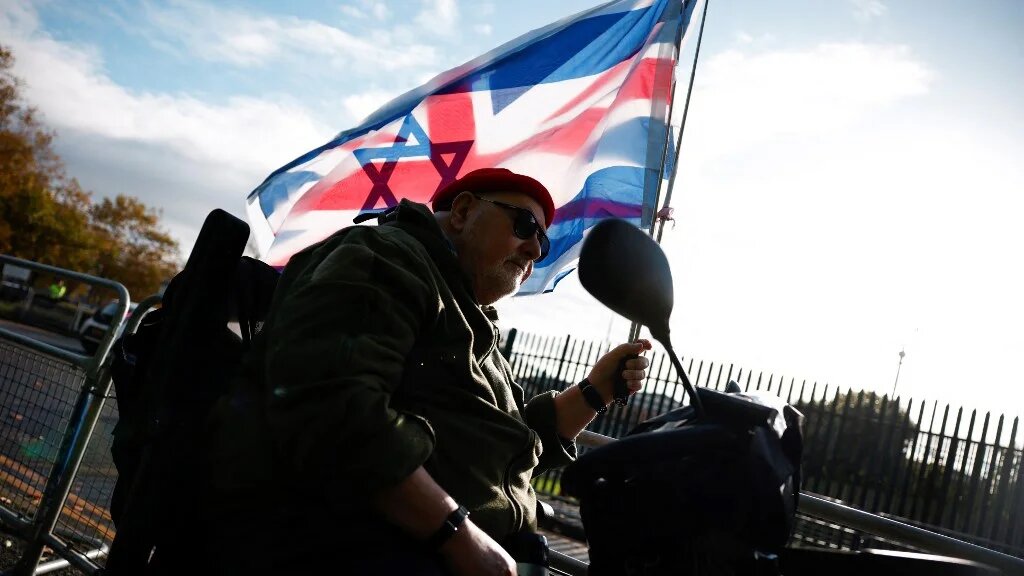 A man waves a Union Jack and an Israeli flag at a demonstration to support British far-right activist Tommy Robinson, in London on 28 October 2024 (Benjamin Cremel/AFP)