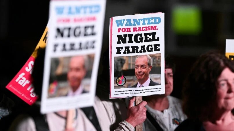 Protesters hold placards denouncing Reform UK leader Nigel Farage during a demonstration in Widnes, northwestern England, on 1 May 2025 (Oli Scarff/AFP)