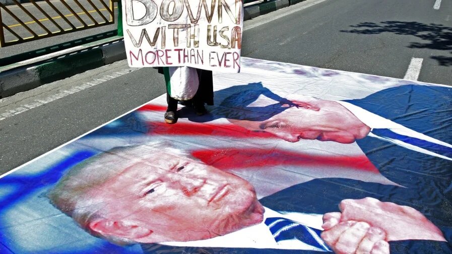 A woman holds a sign while stepping on an image of US President Donald Trump and Israeli Prime Minister Benjamin Netanyahu, in Tehran on 8 June 2018 (AFP)