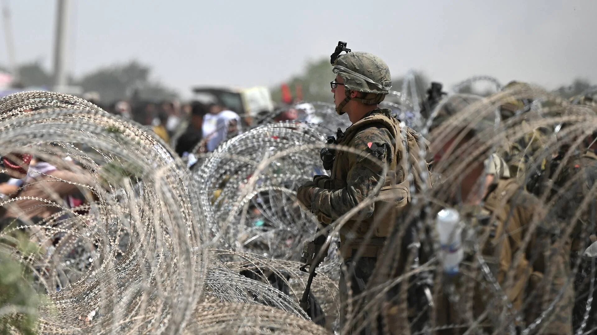 A US soldier stands on guard as Afghans gather on a roadside near the military part of the airport in Kabul on 20 August 2021.