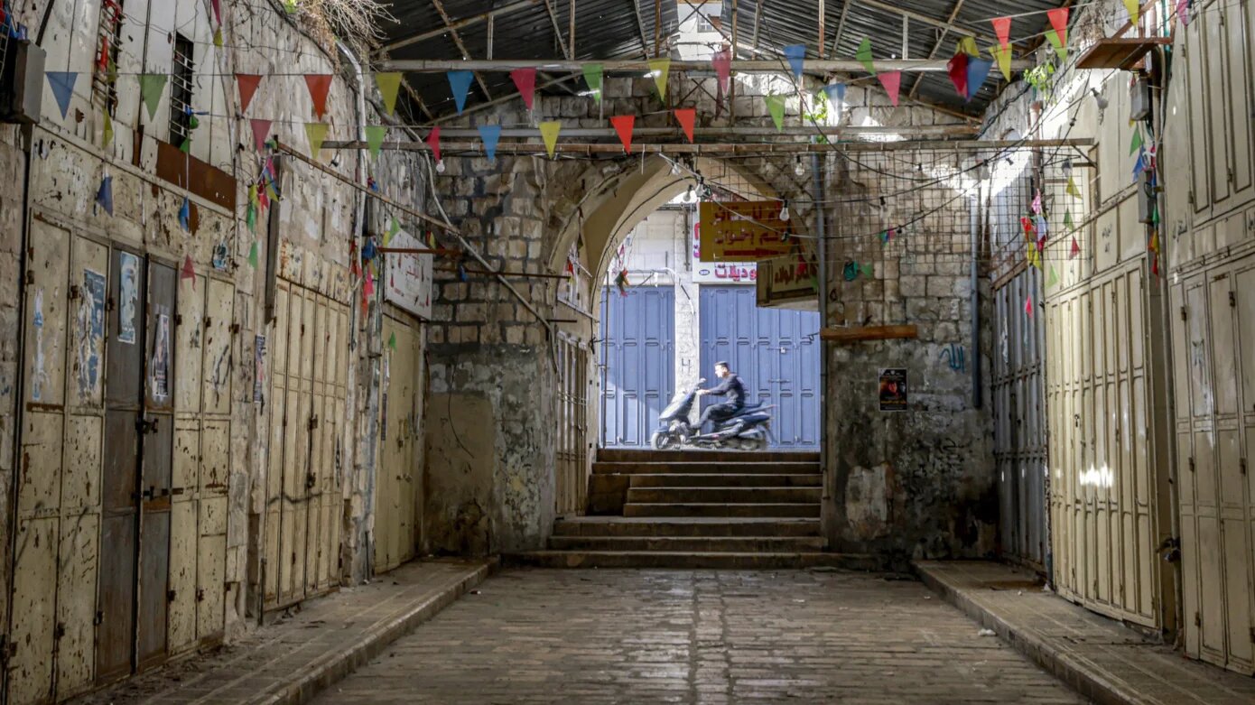 A man rides a motorcycle past an alley with shuttered shops during a general strike in the occupied West Bank city of Nablus on 7 April 2025 (Jaafar Ashtiyeh/AFP)