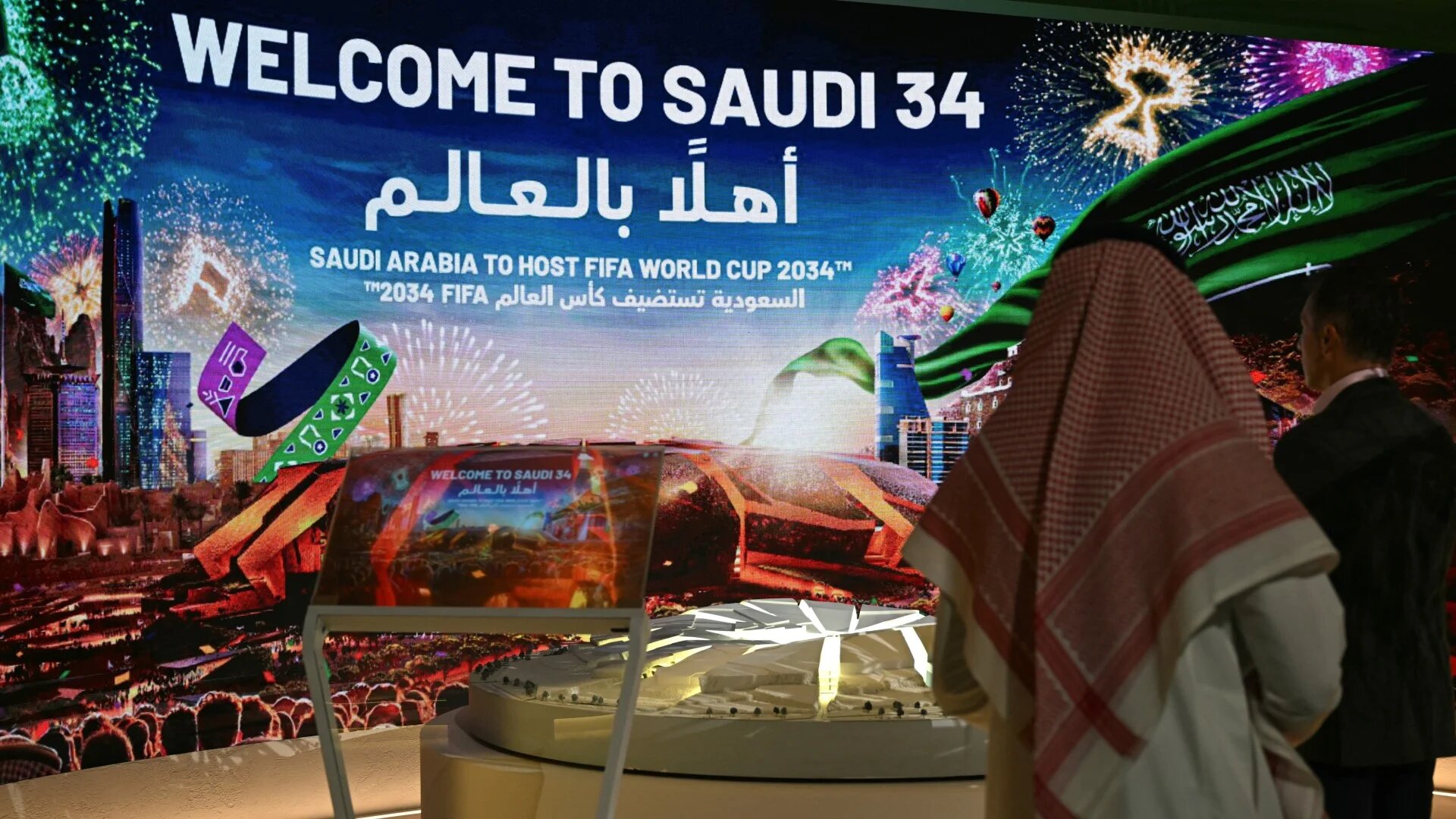 People walk past a stall displaying a welcome message for the Saudi 2034 Fifa World Cup at the Ministry of Media in Riyadh on 13 May 2025 (AFP/Giuseppe Cacace)