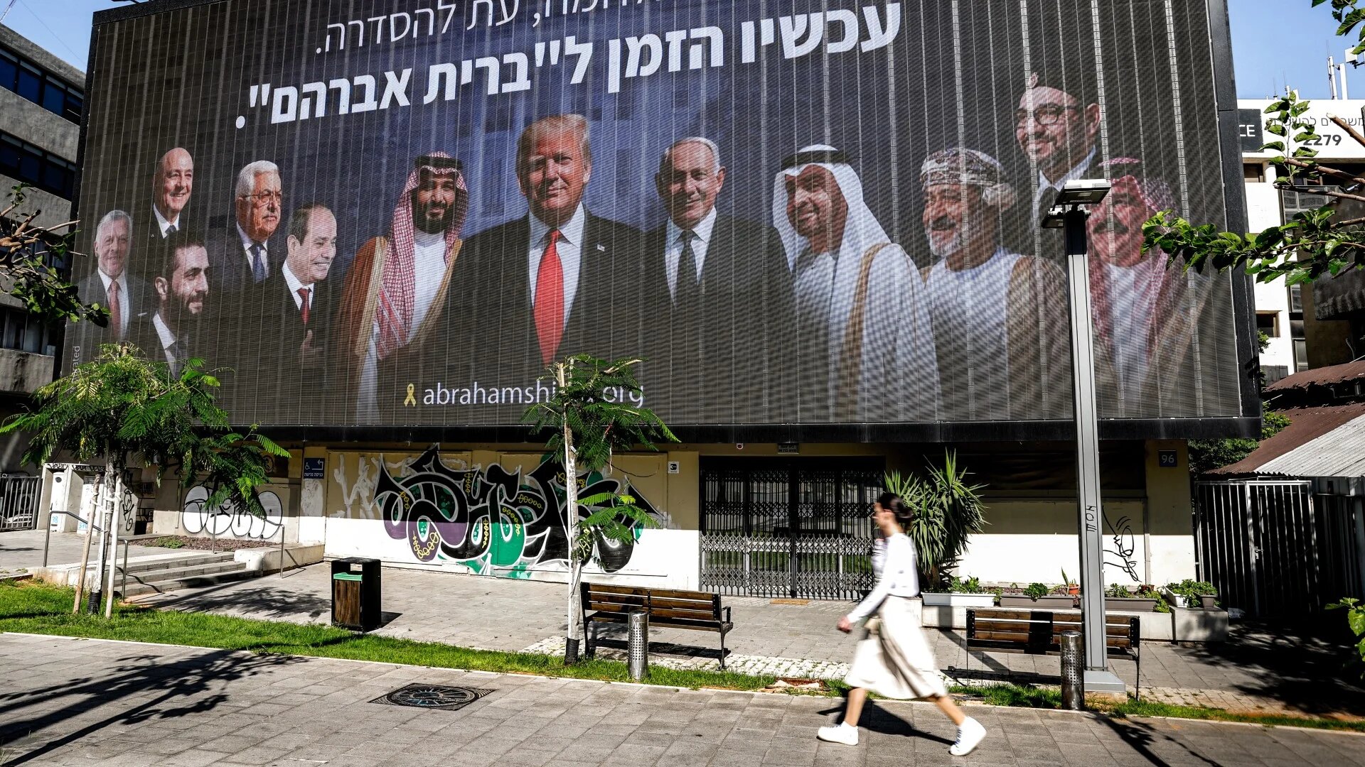 A woman walks past a billboard in Tel Aviv that shows US President Donald Trump, Israel's Prime Minister Benjamin Netanyahu and a host of Arab leaders including Syria's interim president Ahmed al-Sharaa, on 26 June 2025 (Jack Guez/AFP)