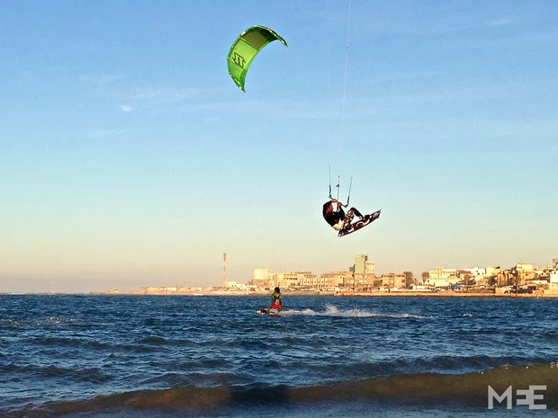 Jalal, one of the country’s more experienced kiters, performing a jump with Tripoli’s skyline in the background (MEE/Tom Wescott)