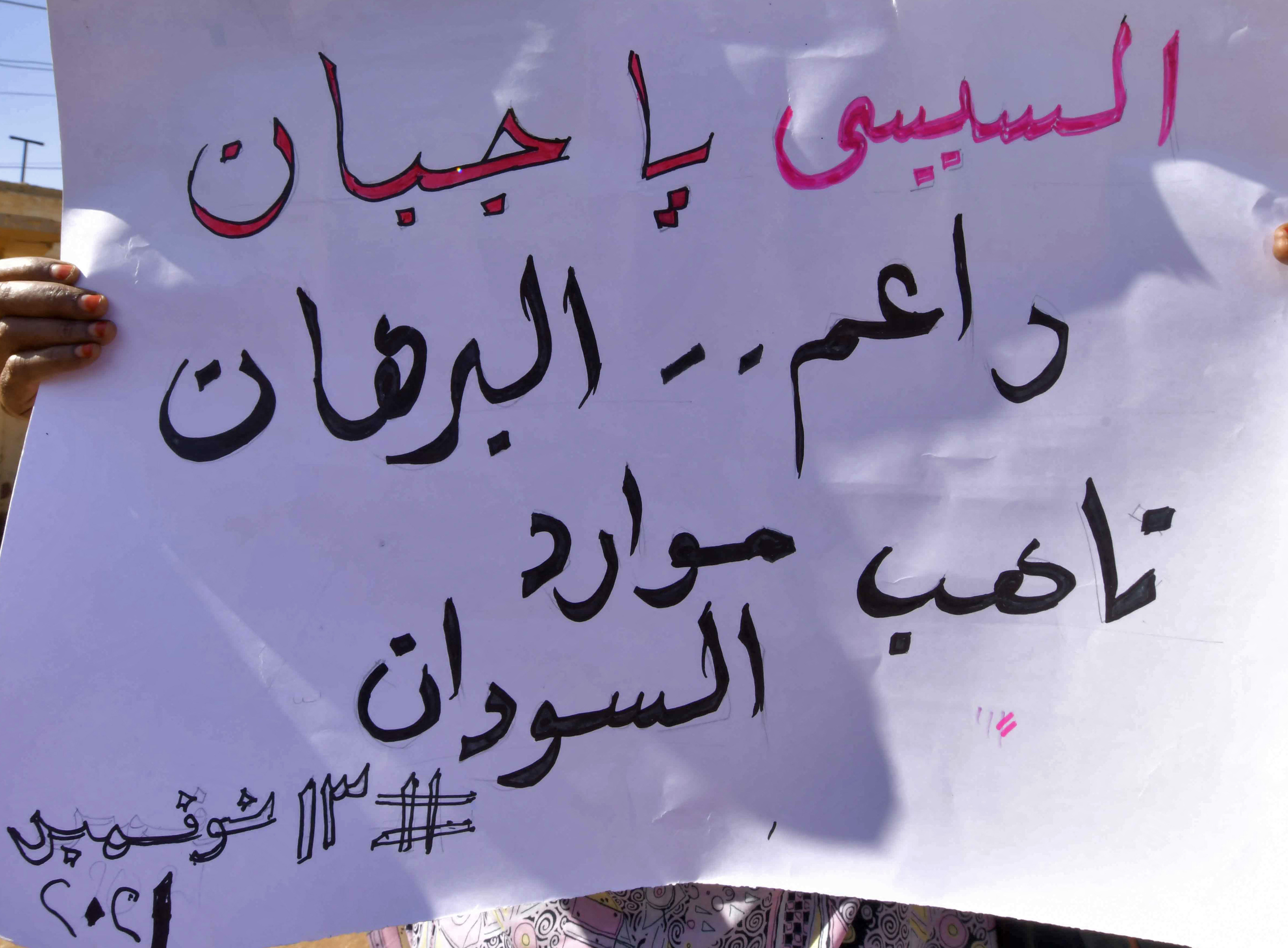 A woman holds a sign raeding in Arabic 