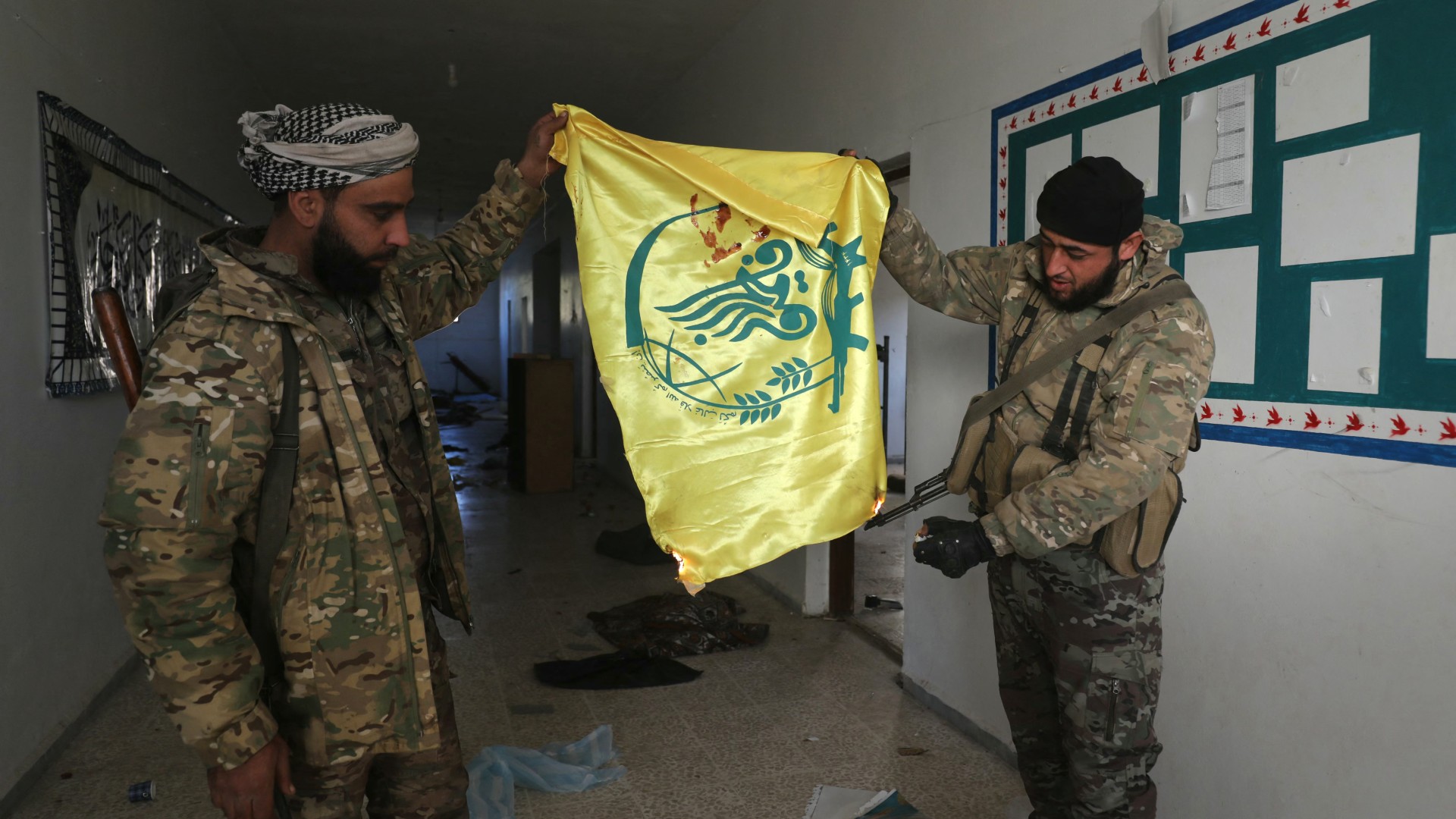 Rebels burn a flag belonging to the Iran-backed Fatemiyoun brigade as they inspect a base in the town of Khan Sheikhun on 1 December 2024 (AFP/Abdulaziz Ketaz)