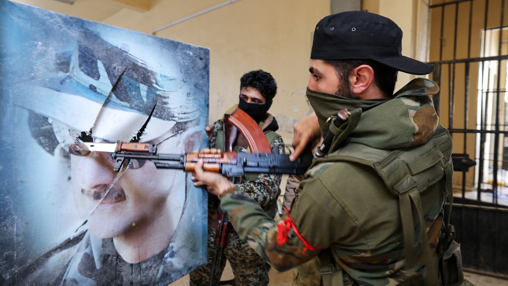 A fighter affiliated with Syria's new administration bayonets a portrait of toppled president Bashar al-Assad at the defunct Mezzeh military prison in Damascus on 2 January 2025 (Anwar Amro/AFP)