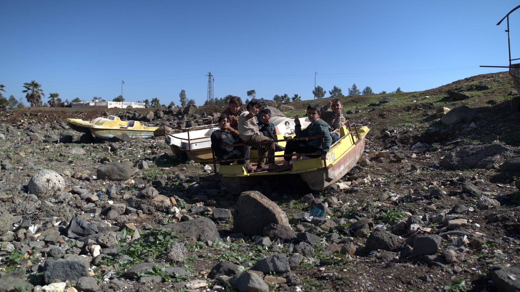 A group of children sit on a small boat in the dry bed of Lake al-Muzayrib, in Syria's Daraa province, in February 2026 (MEE/Saad Kanbar)