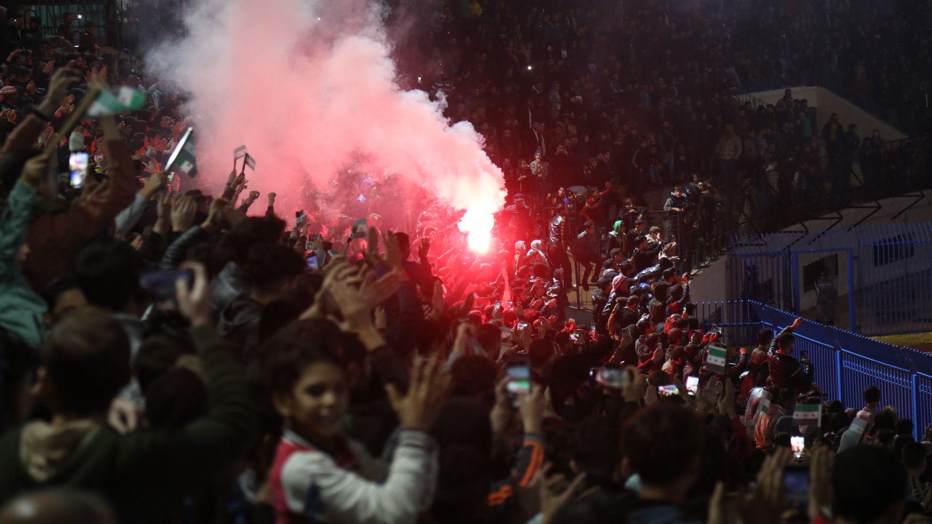 Syrian football fans light a flare during a match at the newly reopened Idlib Municipal Stadium in the rebel-held northwestern Syrian city (MEE/Ali Haj Suleiman)