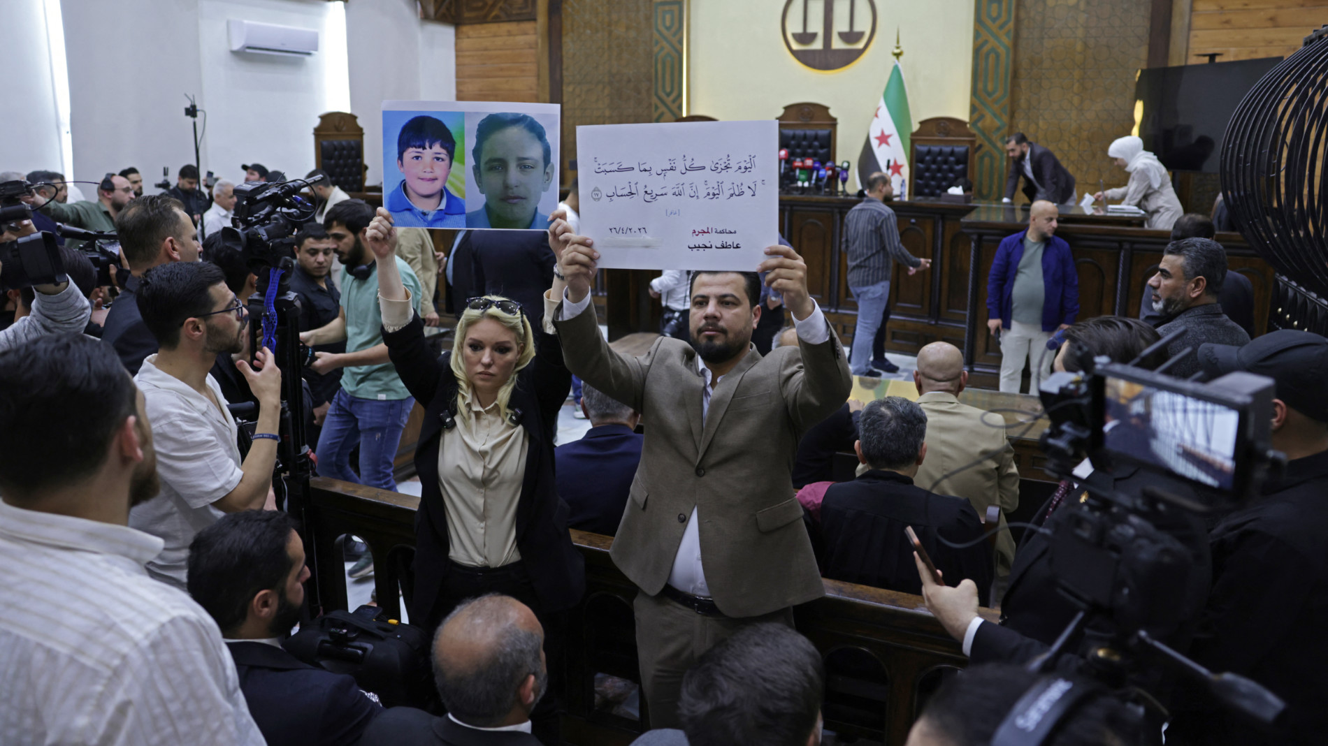 People hold placards at the Palace of Justice ahead of the first trial session, in Damascus on 26 April 2026 (AFP)
