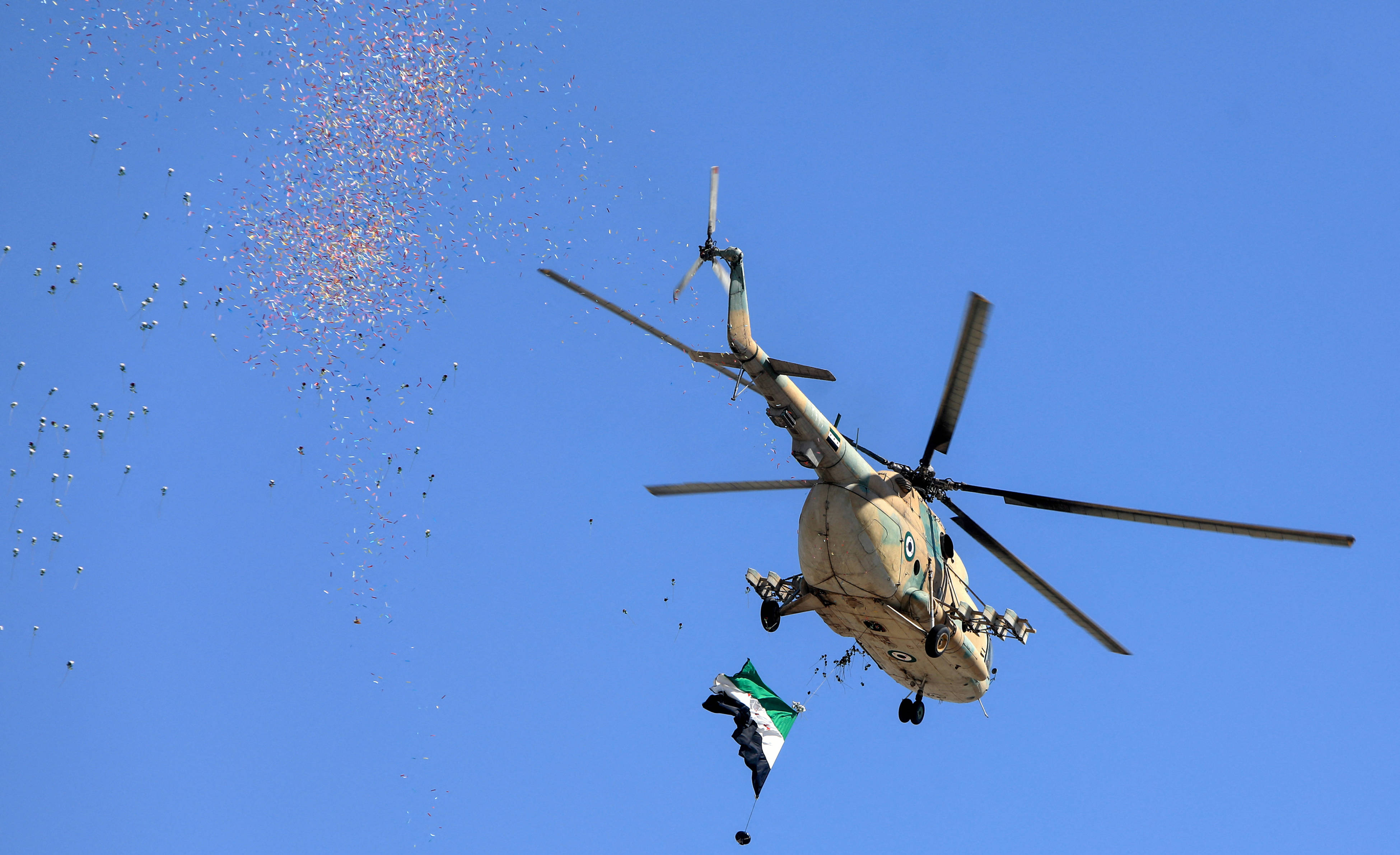 A Syrian security forces helicopter drops confetti and flowers on people celebrating the fourteenth anniversary of Syria's uprising, at a rally in Umayyad Square in Damascus on March 15, 2025 (AFP)