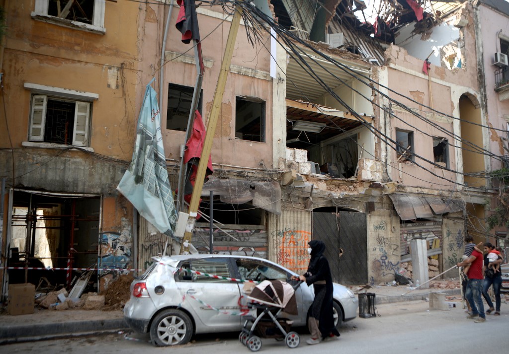 Syrian refugees walk past damaged buildings in the partially destroyed Beirut neighbourhood of Mar Mikhael on 13 August 2020 (AFP)