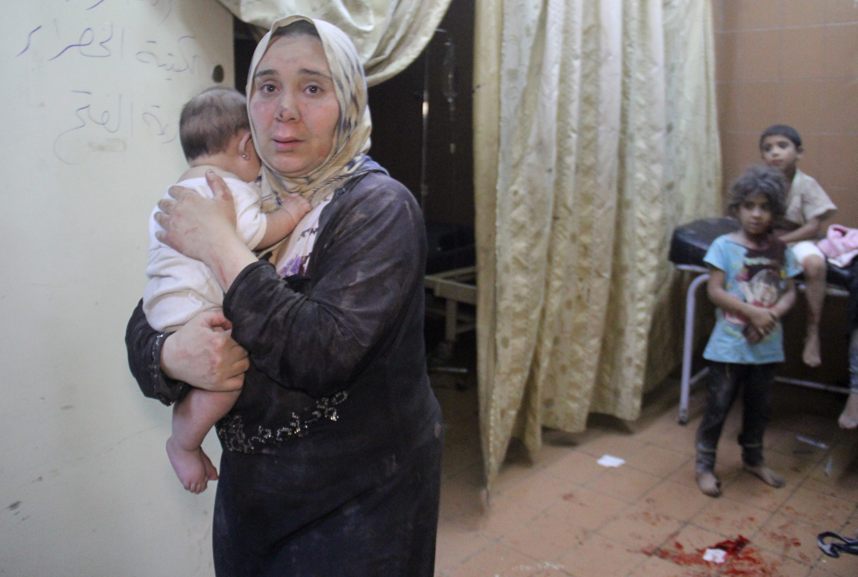 A Syrian woman carries a baby inside a makeshift hospital following strikes and shelling on the rebel-held northwestern city of Idlib, late on 21 July 2016 (AFP)