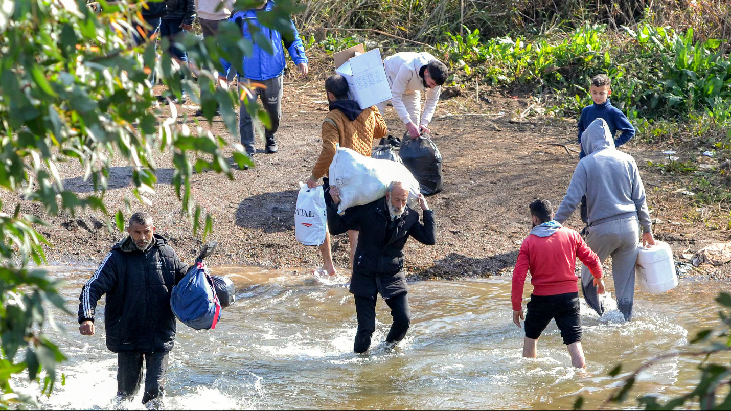 People cross the Nahr al-Kabir river, forming the border between Syria's western coastal province and northern Lebanon in the Hekr al-Daher area on 11 March 2025 (AFP)