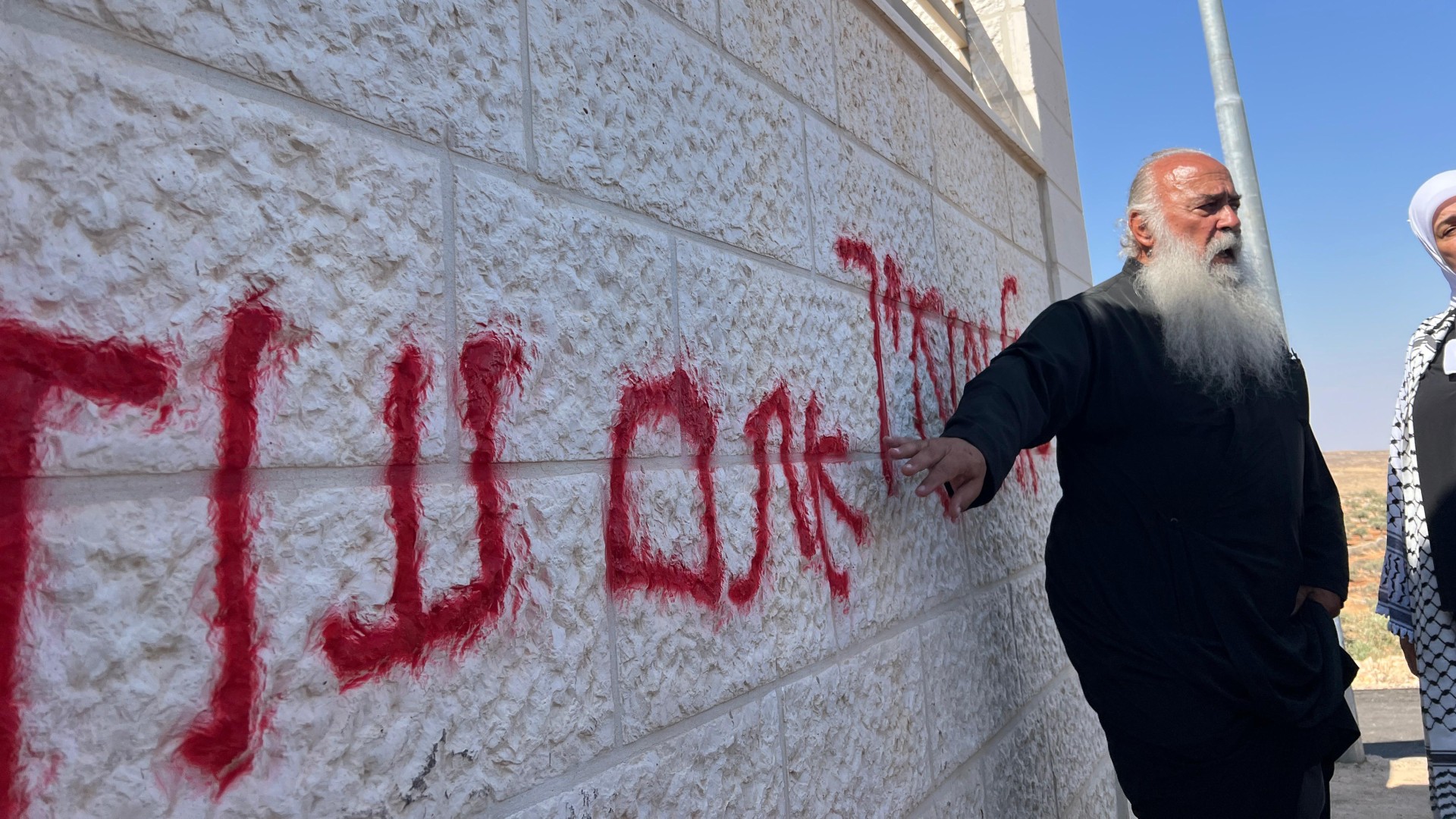 A man beside graffiti painted on a wall in Taybeh by Israeli settlers on 28 July (MEE/Mohammed Turkman)