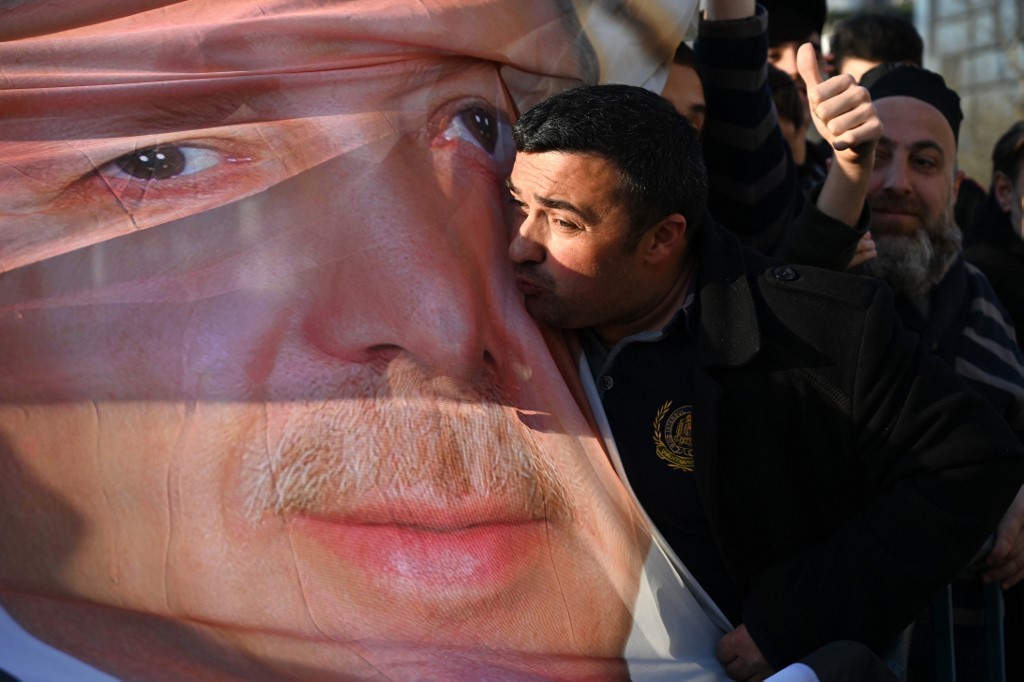 Supporters of ruling Justice and Development Party (AKP) hold a banner picturing Turkish President Recep Tayyip Erdogan while one of them kiss it as they shout slogans during a gathering (AFP)
