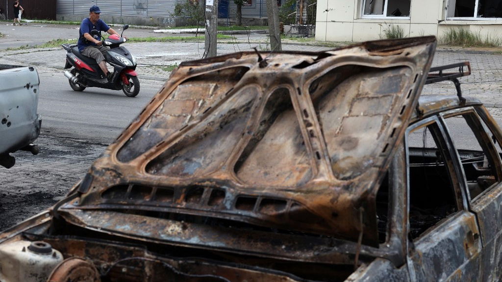 A man drives a scooter past cars destroyed by a cluster missile strike in Lyman, in the Donetsk region of Ukraine, on 8 July 2023 (AFP)