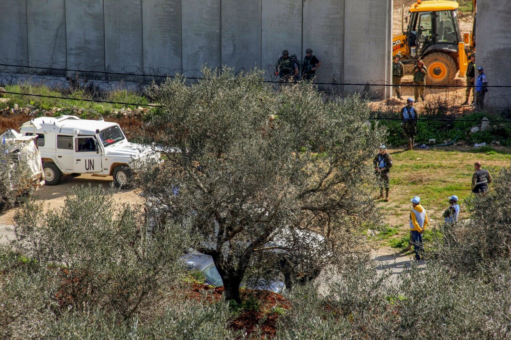 UNIFIL soldiers stand by on 10 March as Israeli soldiers take down a barbed-wire fence after having erected concrete blocks along the border with Lebanon (AFP)