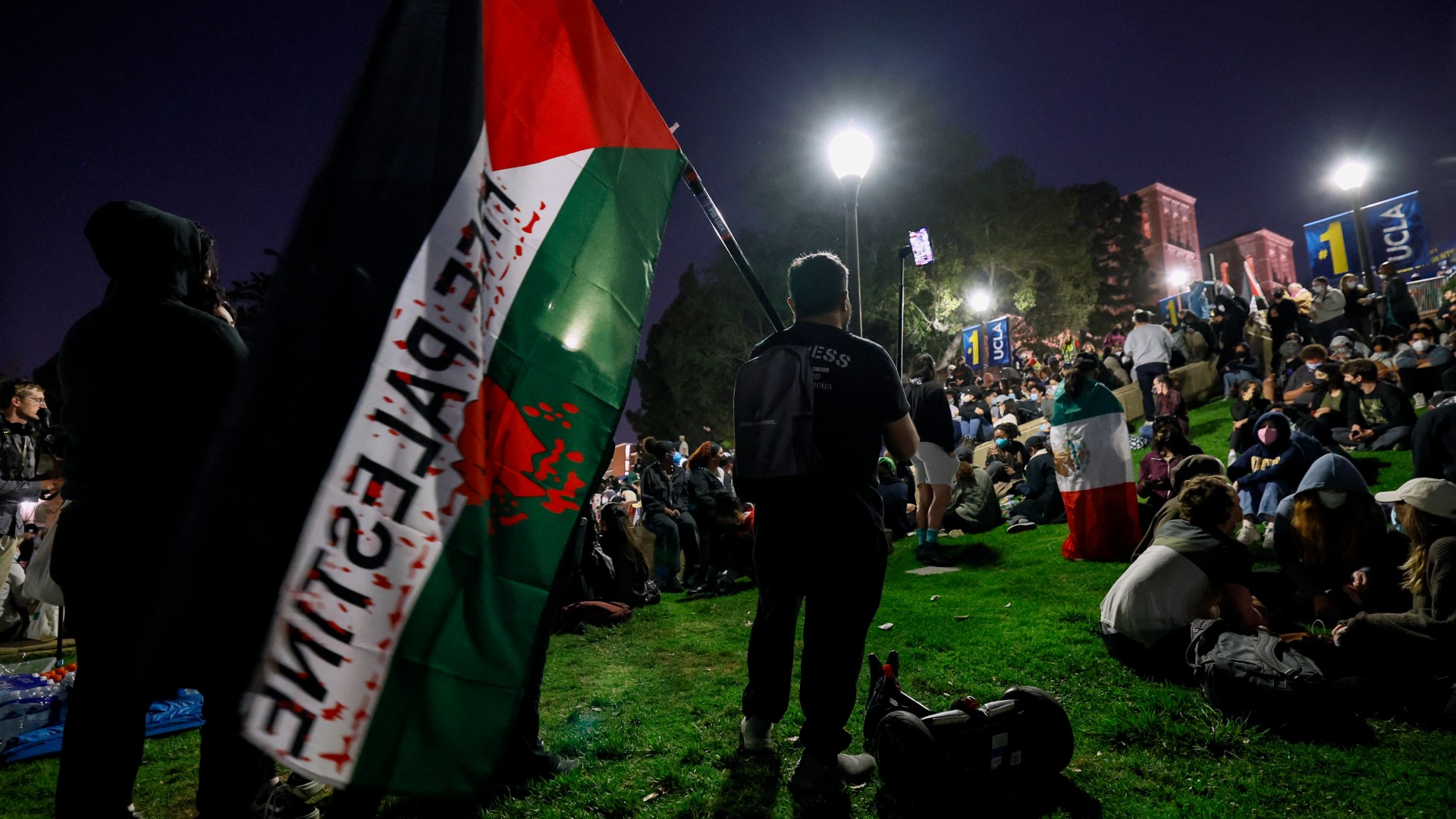 A pro-Palestine protester waves a Palestinian flag at the student encampment at UCLA on 2 May, 2024 (AFP)