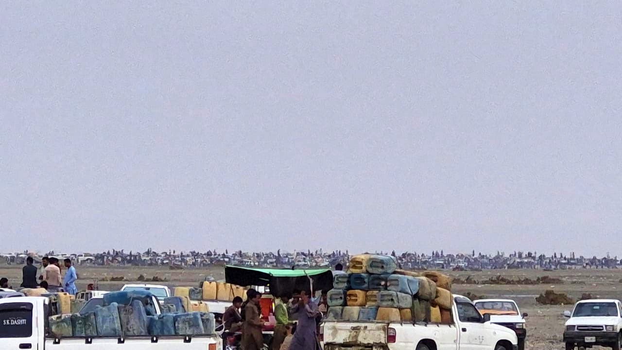 Workers stand beside pickups loaded with fuel containers at Kuntani Hor, while rows of motorcycle transporters gather in the distance