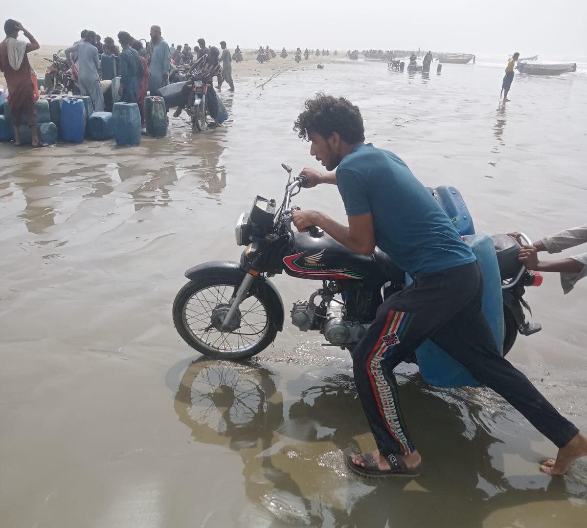 A motorcycle fuel transporter, known locally as a cycali, pulls his loaded bike, carrying two barrels of fuel, out of the muddy shoreline at Kuntani Hor 